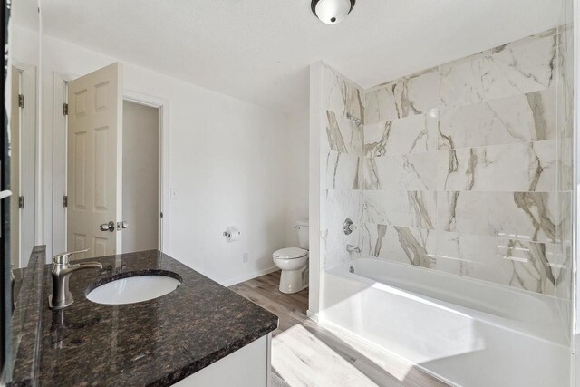 bathroom with baseboards, toilet, vanity, wood finished floors, and washtub / shower combination