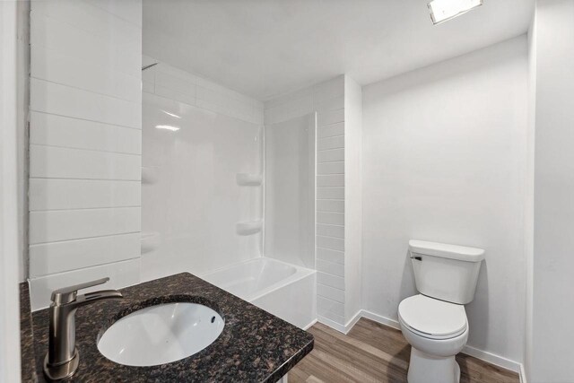 full bath featuring toilet, wood finished floors, baseboards, and a sink