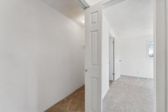 hallway featuring visible vents, a textured ceiling, and carpet flooring