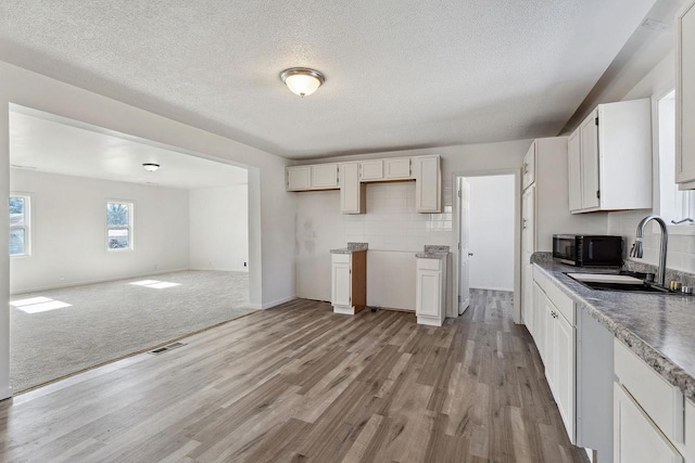 kitchen featuring visible vents, backsplash, black microwave, white cabinetry, and a sink