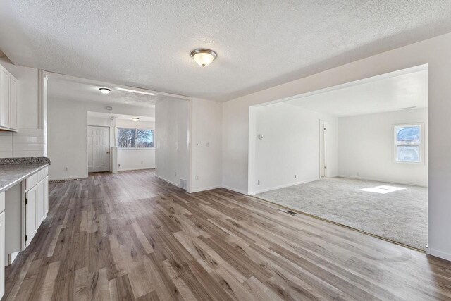unfurnished living room with a wealth of natural light, visible vents, and wood finished floors