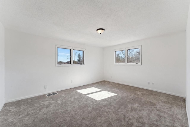 carpeted empty room featuring visible vents, a textured ceiling, and baseboards