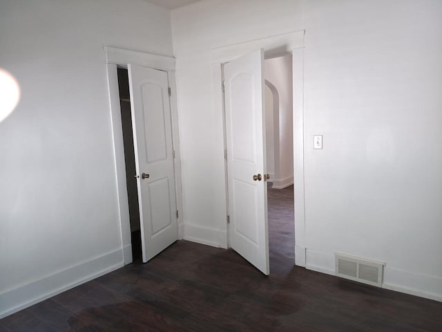 interior space featuring dark wood-style floors, arched walkways, visible vents, and baseboards