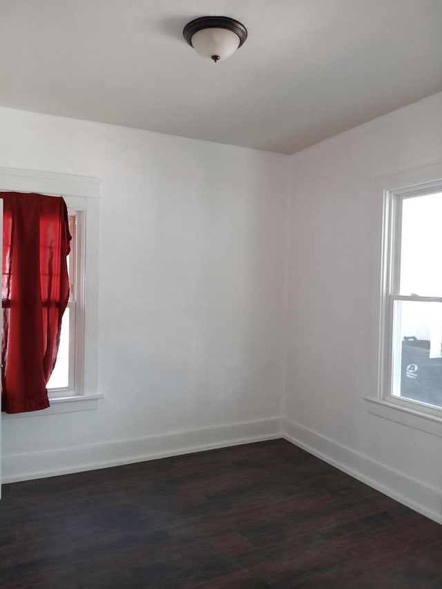 spare room featuring plenty of natural light, baseboards, and dark wood finished floors