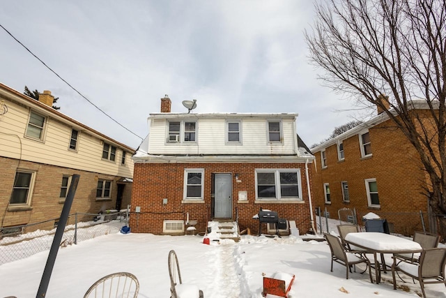 snow covered back of property with entry steps, brick siding, and fence