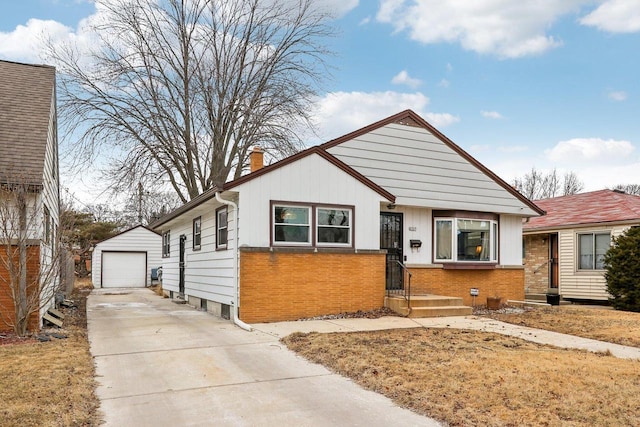 bungalow-style home featuring concrete driveway, a detached garage, a chimney, an outdoor structure, and brick siding