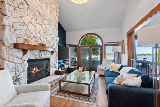 living area with high vaulted ceiling, a stone fireplace, and wood finished floors