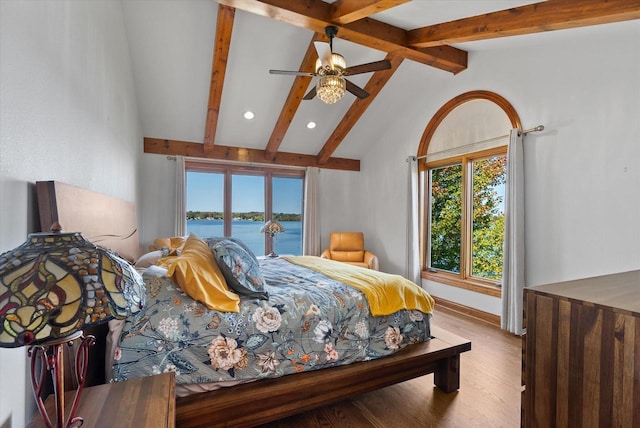 bedroom with a water view, light wood-type flooring, lofted ceiling with beams, and a ceiling fan