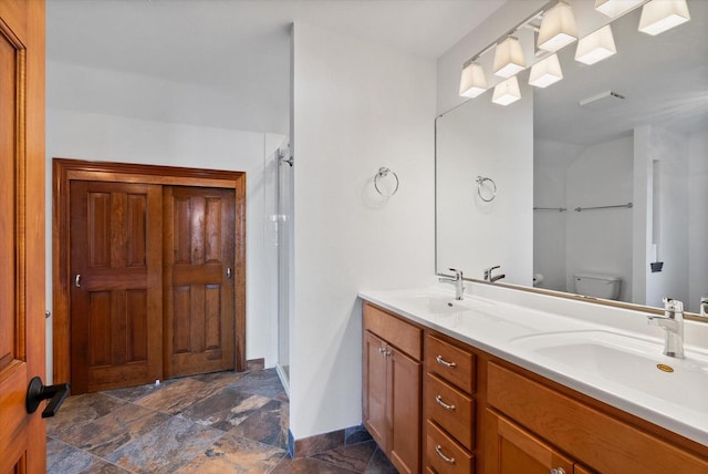 full bathroom featuring stone finish floor, a sink, toilet, and double vanity