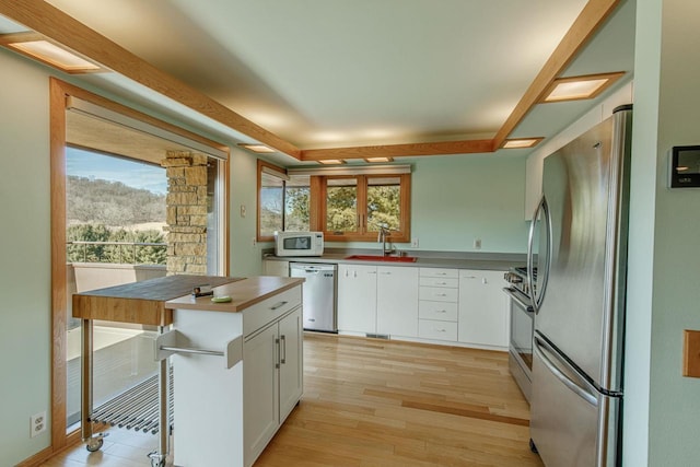 kitchen with light wood finished floors, stainless steel appliances, light countertops, white cabinets, and a sink