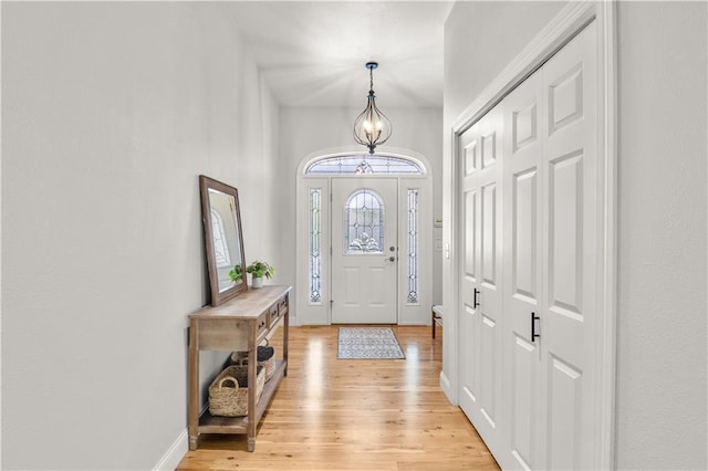 foyer entrance featuring a notable chandelier, baseboards, and light wood-style floors