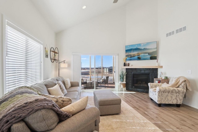 living area with visible vents, a glass covered fireplace, light wood-type flooring, high vaulted ceiling, and recessed lighting