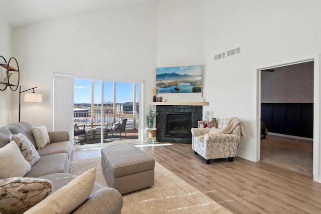 living area featuring a fireplace with flush hearth, light wood-type flooring, visible vents, and a high ceiling