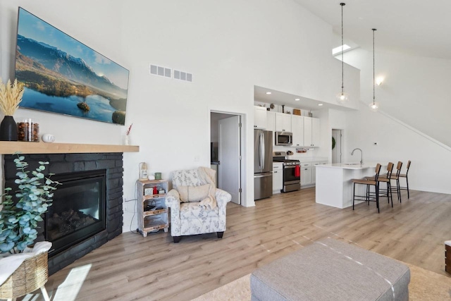 living area featuring light wood-type flooring, visible vents, a fireplace, and lofted ceiling