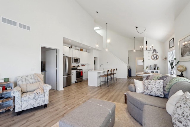 living area with high vaulted ceiling, light wood-style flooring, visible vents, and an inviting chandelier