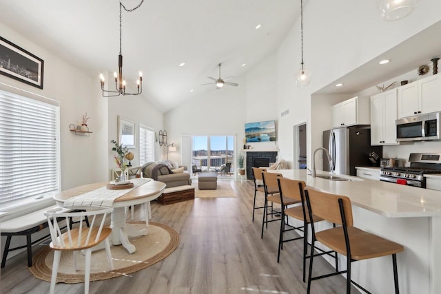 kitchen with a sink, white cabinets, open floor plan, hanging light fixtures, and appliances with stainless steel finishes