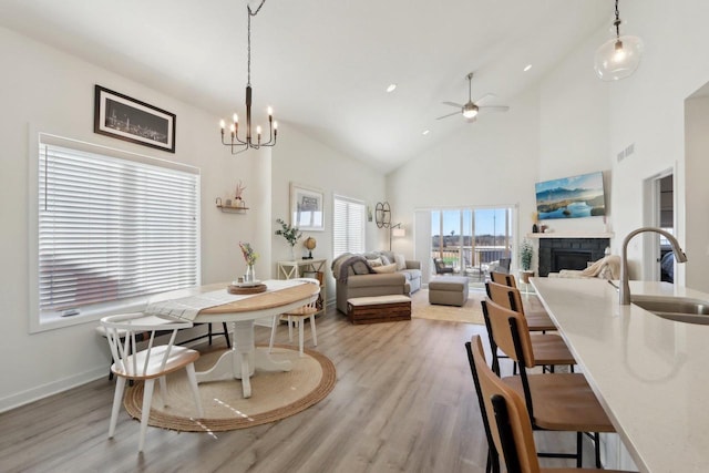 dining room featuring visible vents, a ceiling fan, light wood-style flooring, a fireplace, and high vaulted ceiling