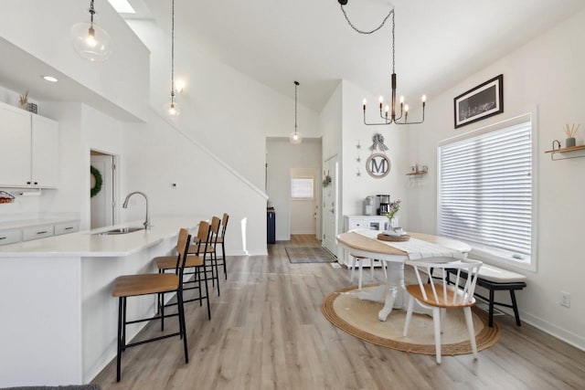 dining room with high vaulted ceiling, a notable chandelier, light wood-style flooring, and baseboards