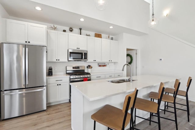 kitchen featuring a center island with sink, stainless steel appliances, light countertops, a sink, and a kitchen bar