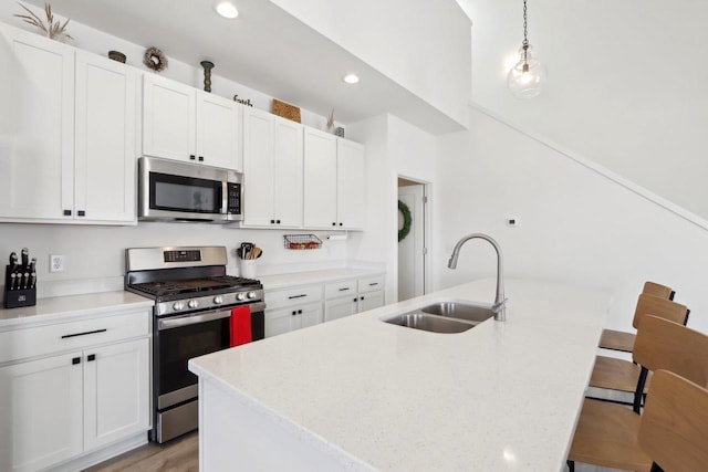 kitchen featuring a kitchen island with sink, stainless steel appliances, a breakfast bar, a sink, and hanging light fixtures