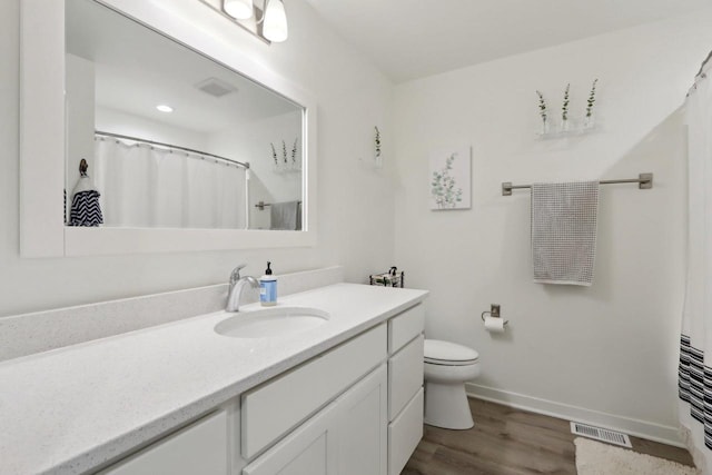 bathroom with visible vents, toilet, vanity, wood finished floors, and baseboards