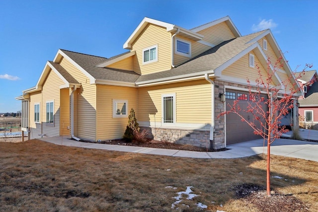 back of house with a shingled roof, stone siding, driveway, and an attached garage