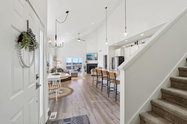 foyer entrance featuring high vaulted ceiling, a fireplace, visible vents, light wood-style floors, and stairway