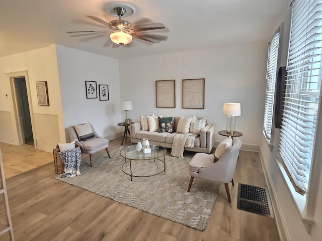 living area featuring a ceiling fan, light wood-type flooring, visible vents, and baseboards