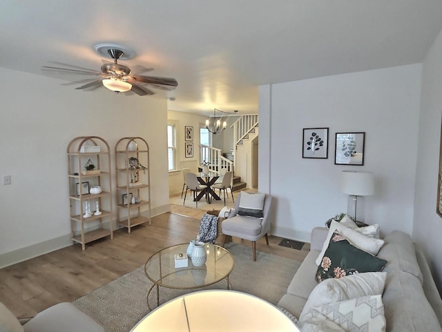 living area featuring ceiling fan with notable chandelier, wood finished floors, baseboards, and stairs