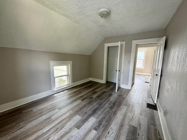 bonus room with dark wood-style floors, baseboards, visible vents, and vaulted ceiling