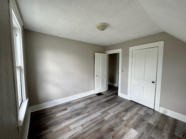 unfurnished bedroom featuring lofted ceiling, a textured ceiling, baseboards, and wood finished floors