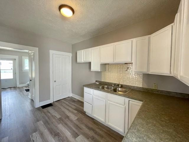 kitchen featuring dark countertops, white cabinetry, a sink, and backsplash