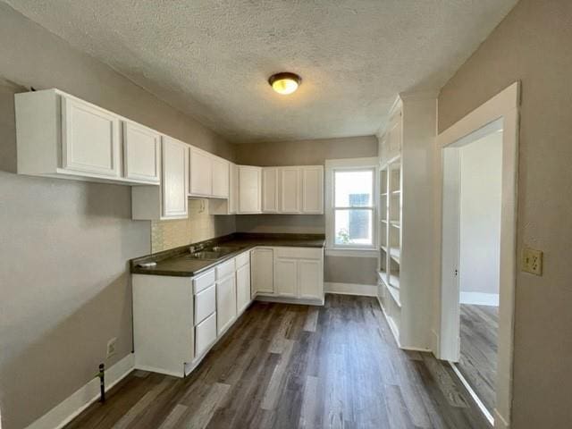 kitchen featuring baseboards, white cabinets, dark wood finished floors, dark countertops, and a textured ceiling