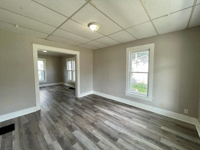 empty room with dark wood-style floors, a drop ceiling, visible vents, and baseboards