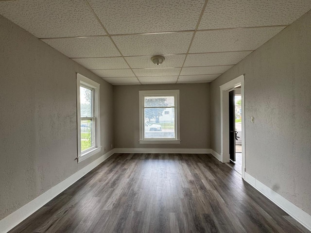 spare room with dark wood-style floors, a textured wall, a drop ceiling, and baseboards