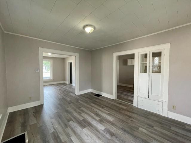 empty room with dark wood-style floors, ornamental molding, and baseboards