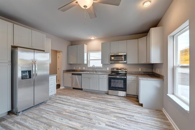 kitchen featuring light wood finished floors, baseboards, stainless steel appliances, white cabinetry, and a sink