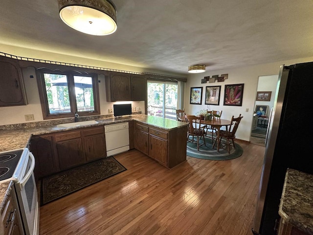 kitchen featuring a peninsula, white appliances, a sink, and wood finished floors