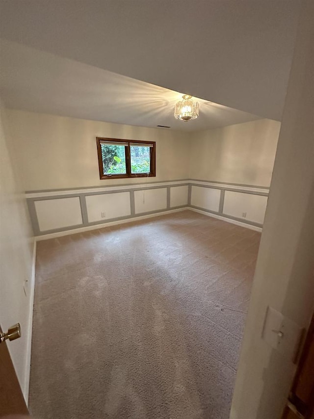 carpeted spare room featuring a wainscoted wall, an inviting chandelier, and a decorative wall