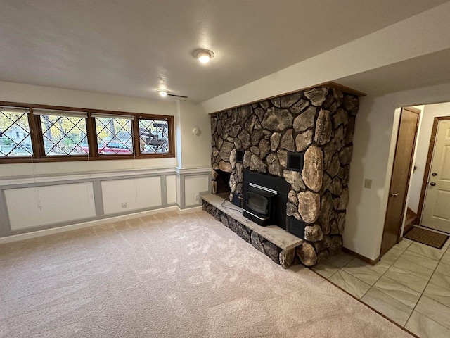 unfurnished living room featuring a decorative wall, wainscoting, light tile patterned flooring, and light colored carpet