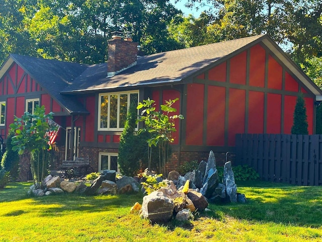 view of home's exterior with a yard, brick siding, a chimney, and fence