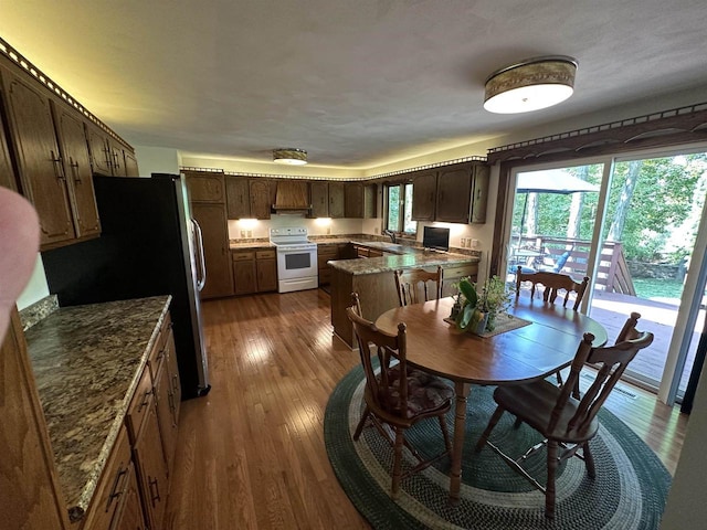 interior space with white electric range, dark wood-type flooring, freestanding refrigerator, stone countertops, and a kitchen island