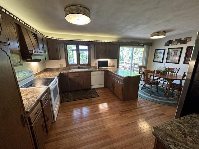 kitchen featuring dark brown cabinetry, a peninsula, white appliances, a sink, and dark wood-style floors