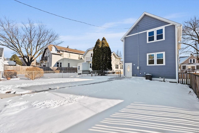 snow covered property with central AC and fence