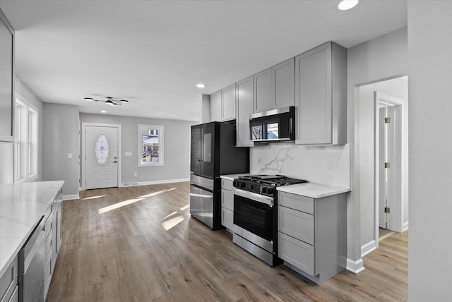 kitchen featuring light stone counters, appliances with stainless steel finishes, light wood-type flooring, gray cabinets, and decorative backsplash