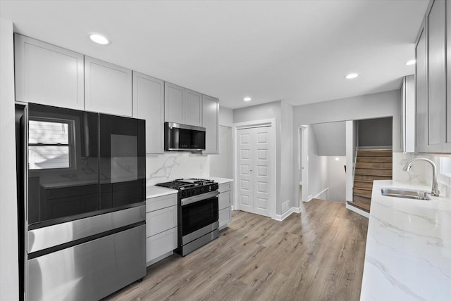 kitchen featuring tasteful backsplash, light wood-style flooring, light stone counters, stainless steel appliances, and a sink