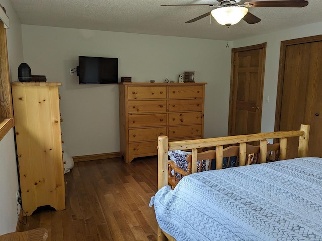 bedroom with a textured ceiling, ceiling fan, dark wood-style flooring, baseboards, and two closets