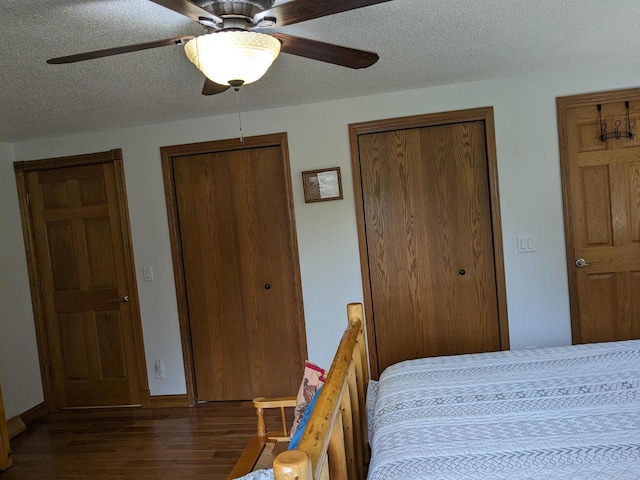 bedroom with a textured ceiling, dark wood-type flooring, two closets, and a ceiling fan