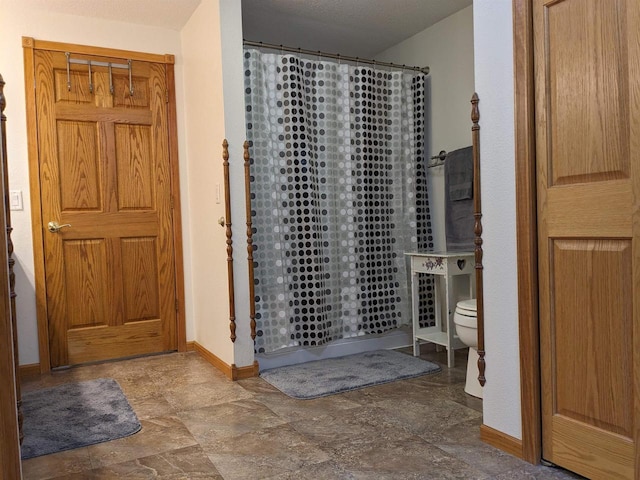 bathroom featuring stone finish flooring, a shower with curtain, toilet, and baseboards