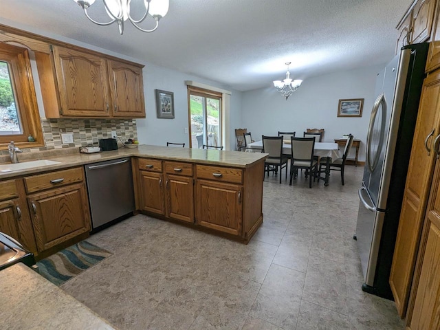 kitchen with appliances with stainless steel finishes, brown cabinets, a peninsula, an inviting chandelier, and light countertops